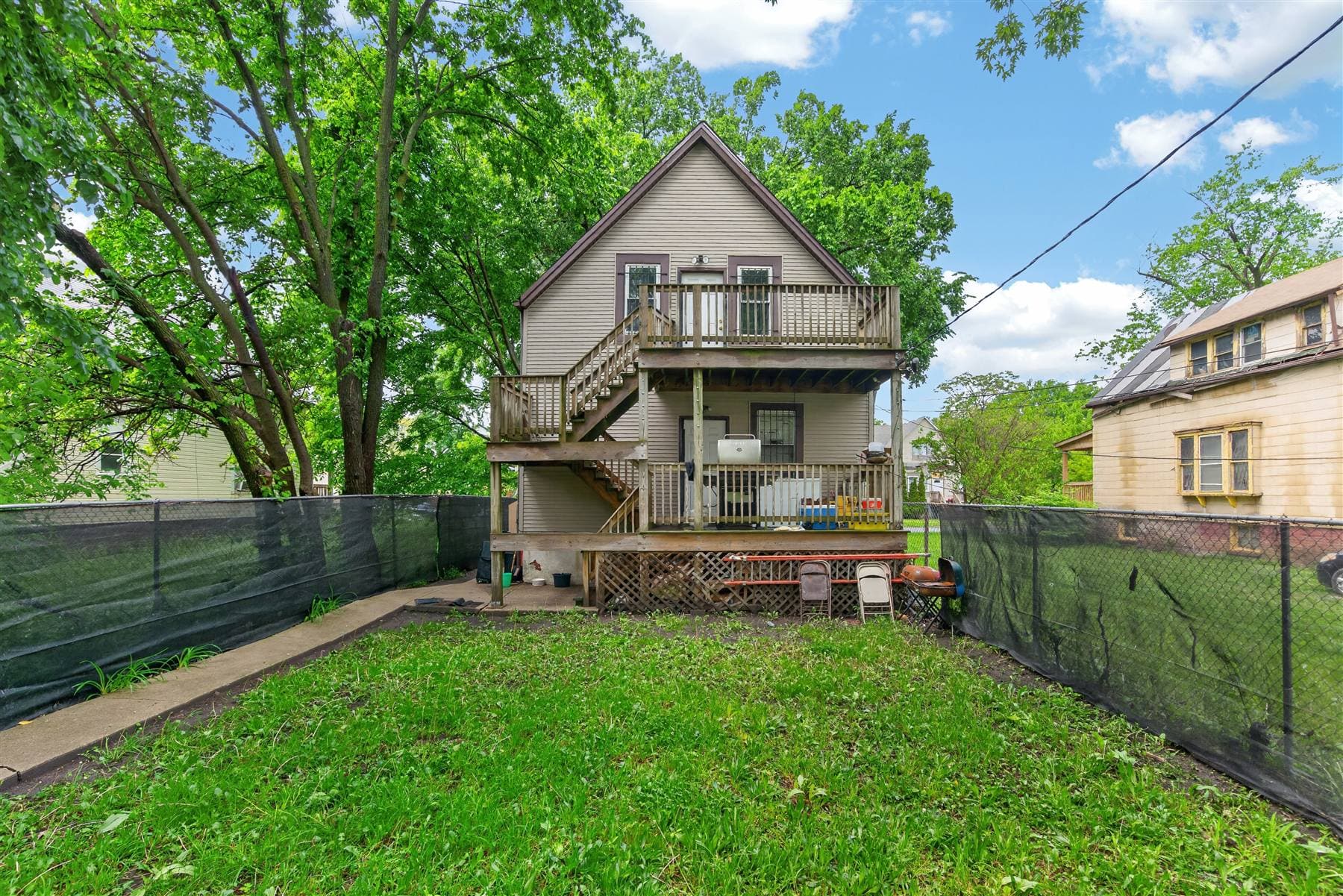 Rear exterior real estate photo showing a fenced backyard, deck, and mature trees